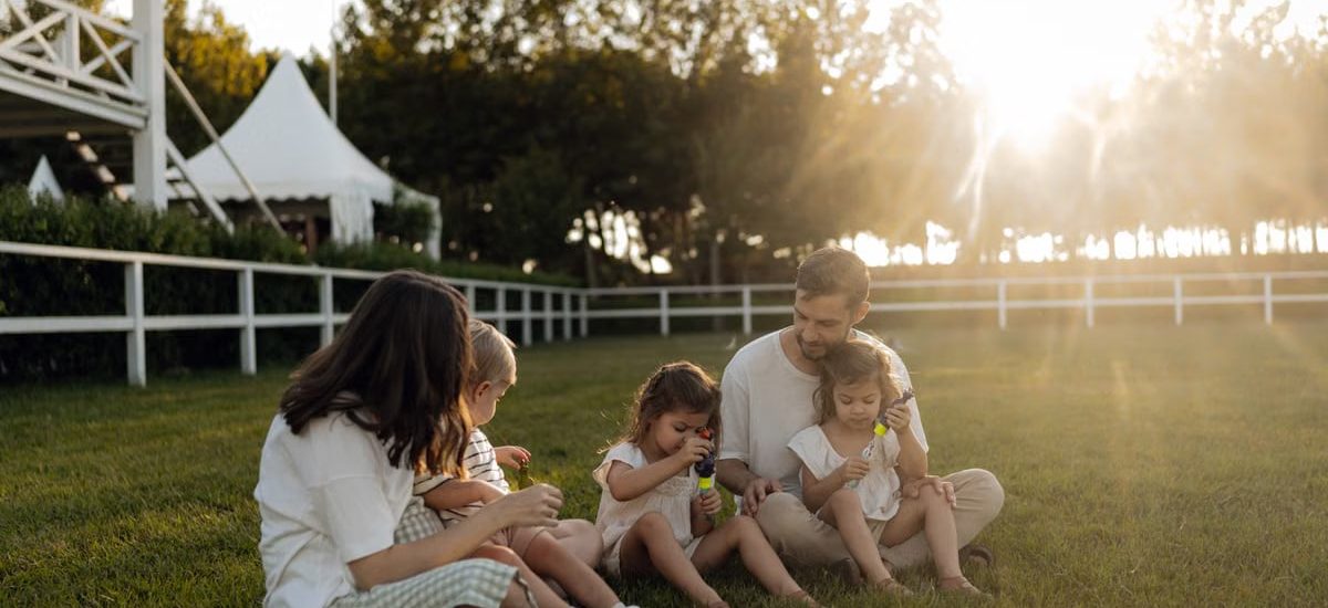 Family sitting on grass enjoying leisure time outdoors, with sun setting in the background.